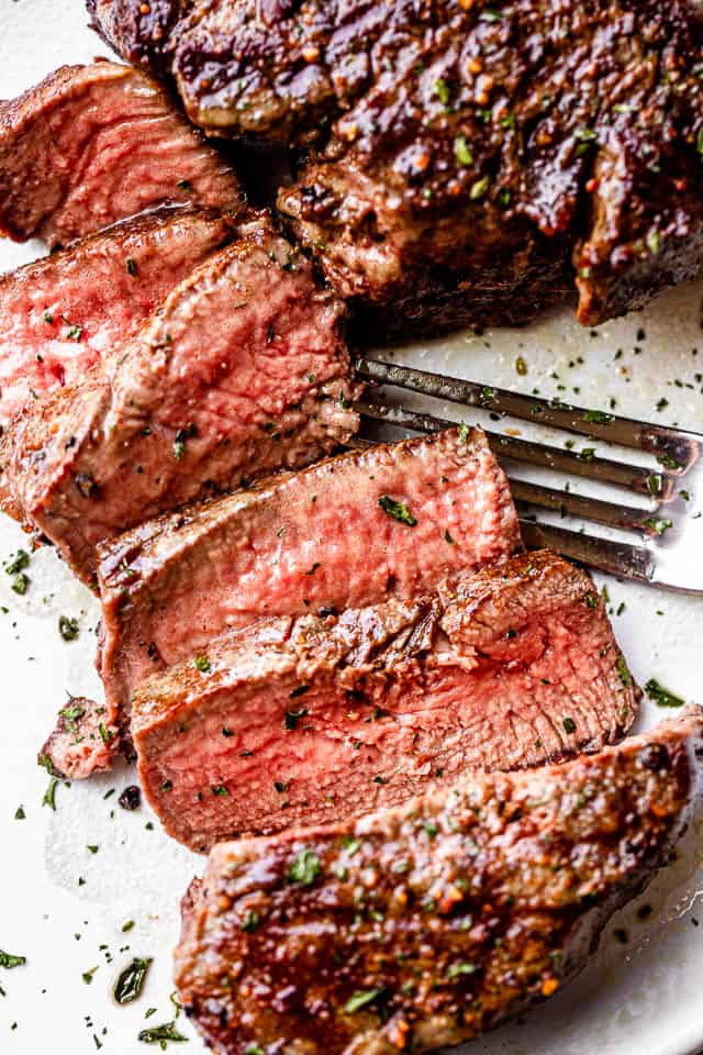 Sliced filet mignon on a plate next to a fork.