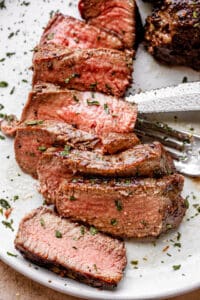 Slicked filet mignon on a plate next to a fork and knife