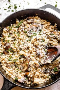 top view of a skillet filled with cauliflower rice and mushrooms topped with asiago cheese