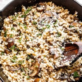 top view of a skillet filled with cauliflower rice and mushrooms topped with asiago cheese