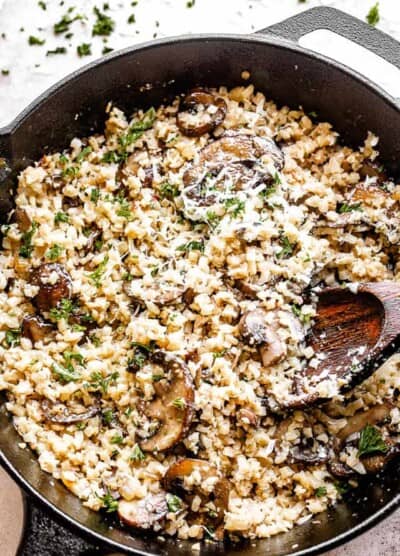 top view of a skillet filled with cauliflower rice and mushrooms topped with asiago cheese