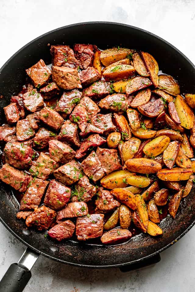 Steak bites and potatoes in a black skillet.