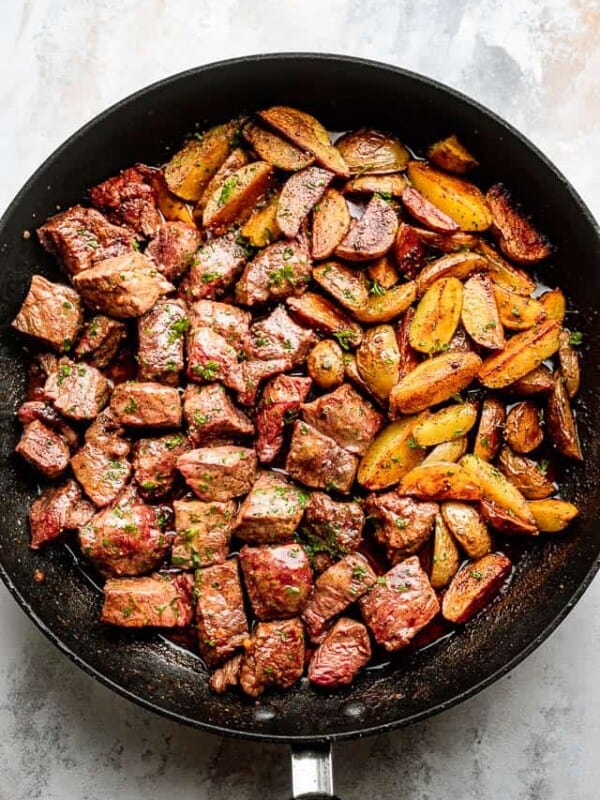 Overhead shot of a black skillet with steak bites and fried potatoes.