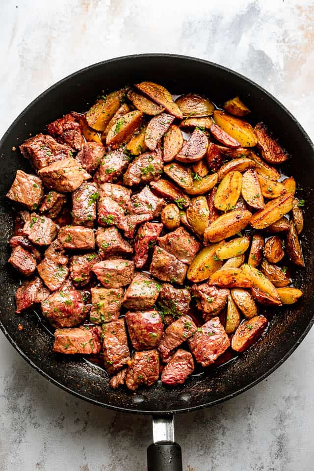 overhead shot of a black skillet with steak bites and fried potatoes