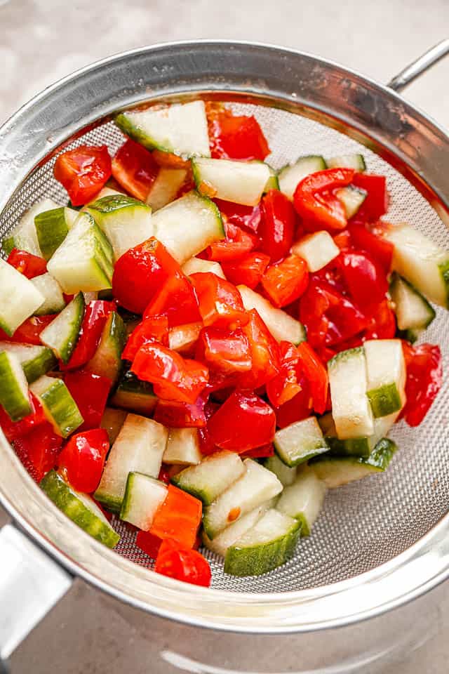 draining tomatoes and cucumbers in a mesh strainer