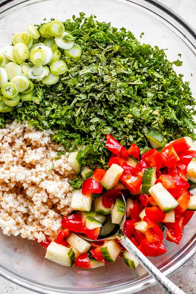 A glass bowl with bulgur, cucumber, tomatoes and parsley