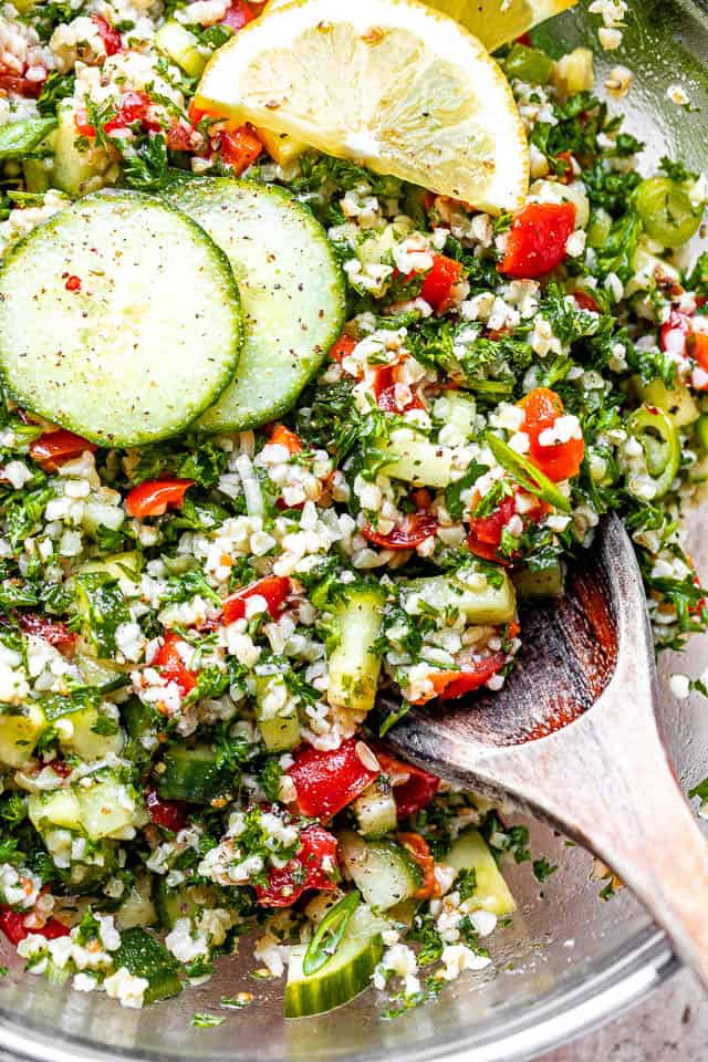 tabbouleh salad topped with sliced cucumbers and lemons and a wooden spoon on the side.