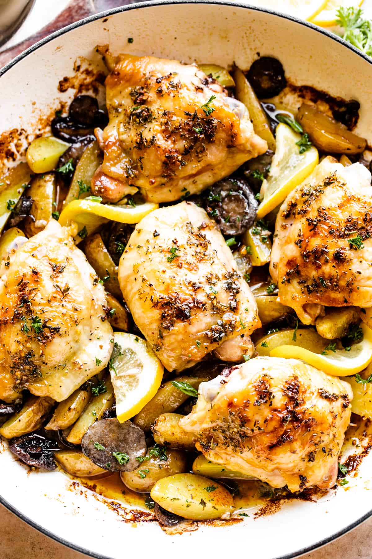 up close photo of garlic butter baked chicken thighs atop potatoes and mushrooms