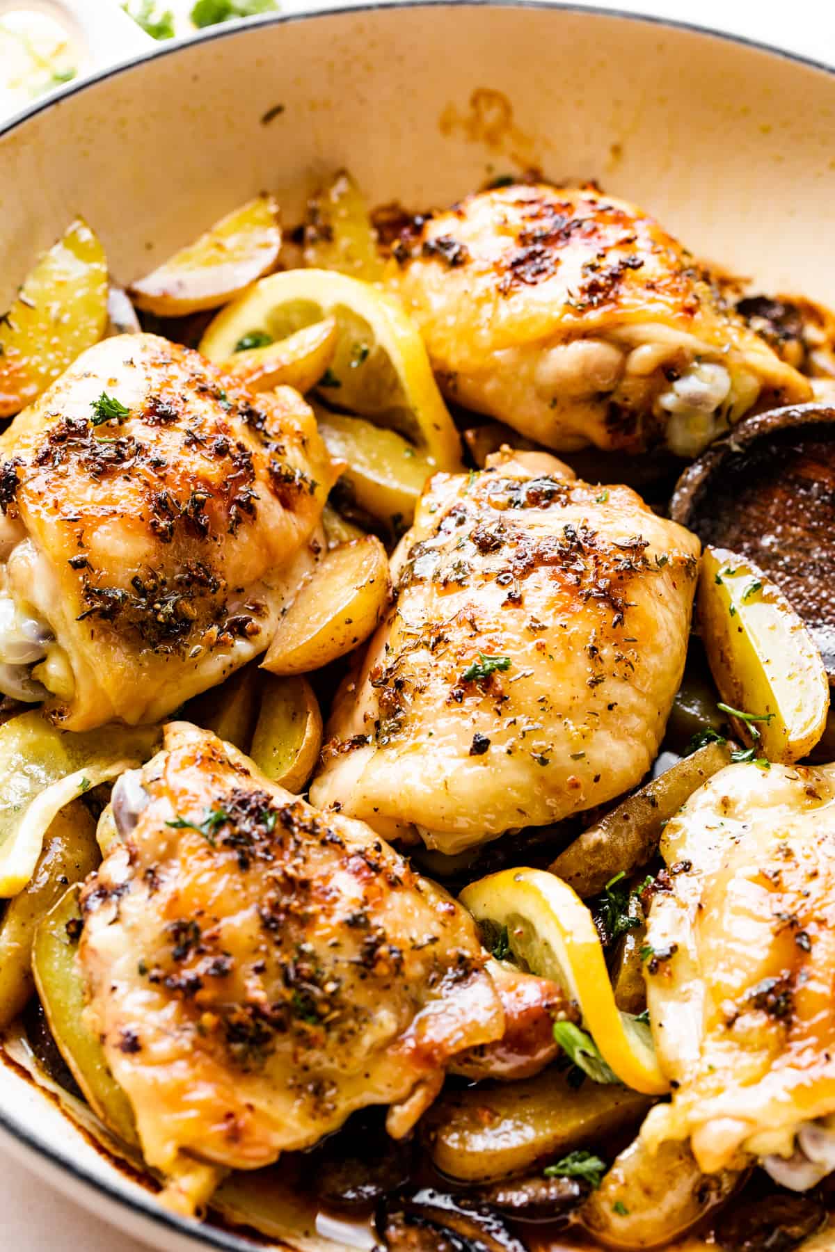 up close photo of garlic butter baked chicken thighs atop potatoes and mushrooms