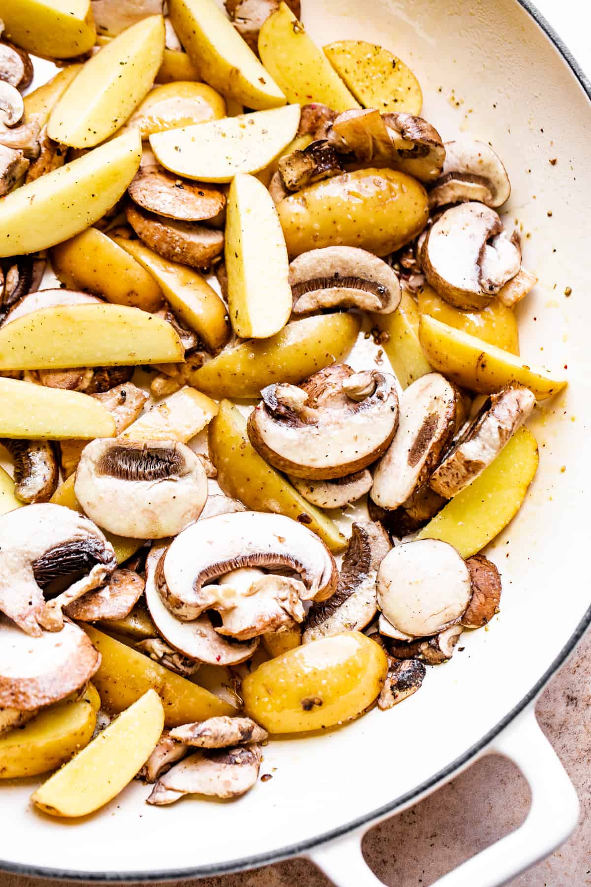 cooking potatoes and mushrooms in a white ceramic skillet.