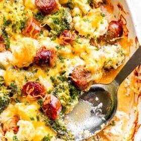 big silver spoon set inside a cheesy cauliflower broccoli casserole studded with slices of smoked sausage
