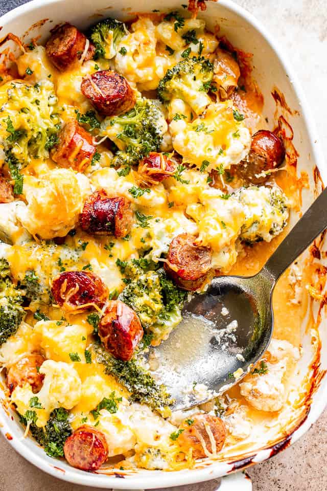 big silver spoon set inside a cheesy cauliflower broccoli casserole studded with slices of smoked sausage