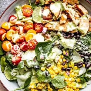 chicken strips, corn, tomatoes, and black beans set over salad greens in a salad bowl and drizzled with avocado salad dressing