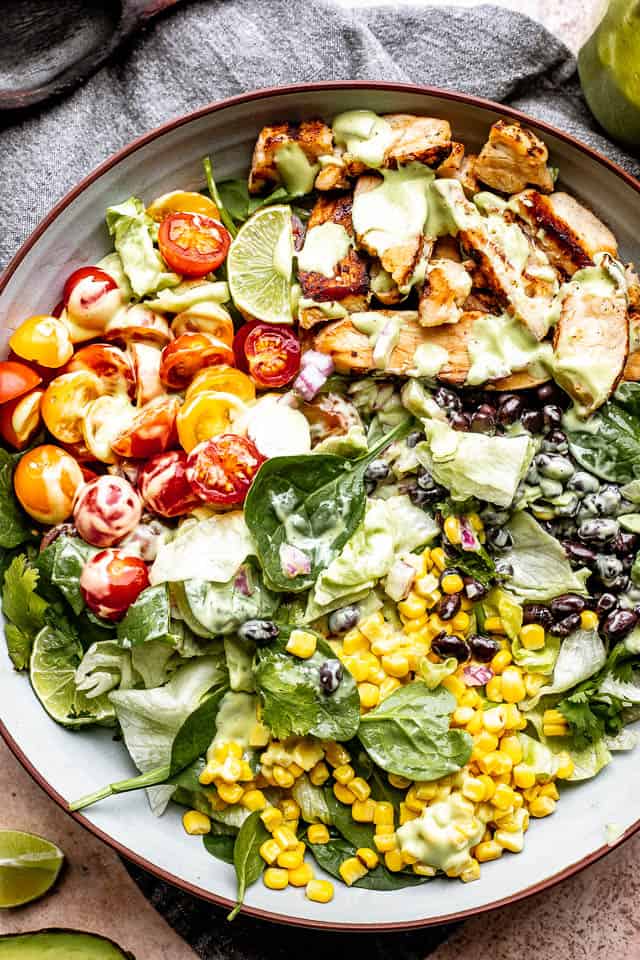 chicken strips, corn, tomatoes, and black beans set over salad greens in a salad bowl and drizzled with avocado salad dressing