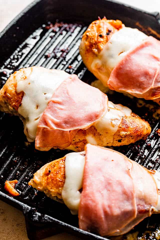 three ham and cheese topped chicken breasts on a grill pan