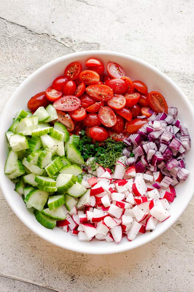 chopped red onions, cucumbers, tomatoes, radishes, and herbs in a bowl