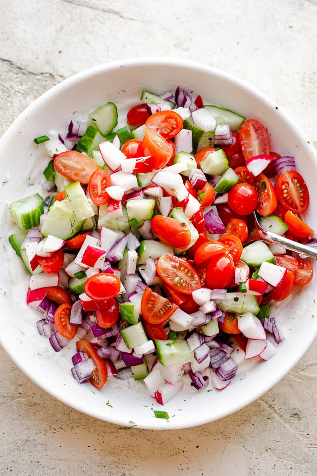 a mound of chopped cucumbers, tomatoes, and radishes inside of a white bowl