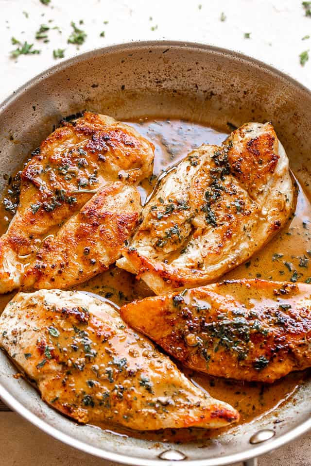 four chicken breasts cooking in a stainless steel skillet