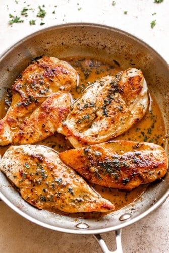 four chicken breasts cooking in a stainless steel skillet