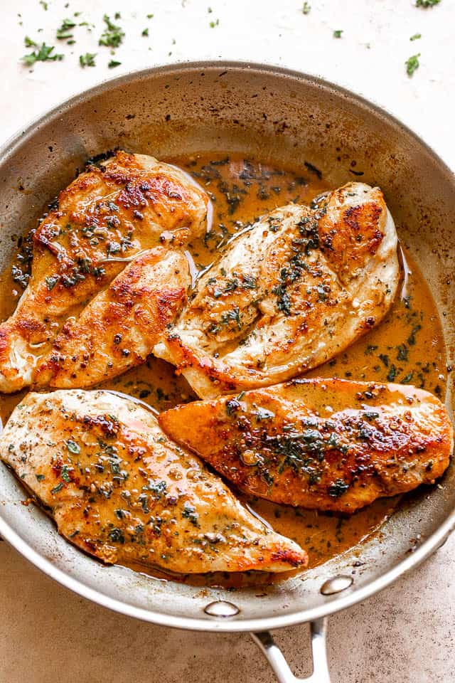 four chicken breasts cooking in a stainless steel skillet