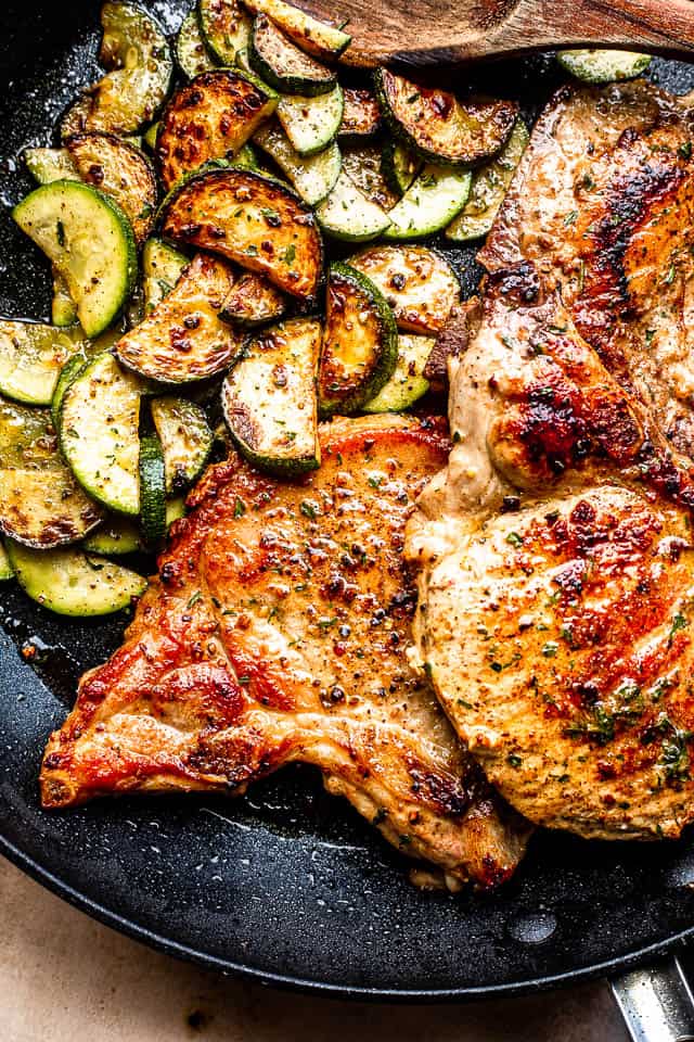 closeup of pork chops and zucchini slices in a black skillet