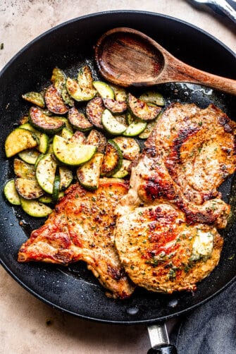 cooked sliced zucchini and cooked pork chops in a skillet with wooden spoon to the side