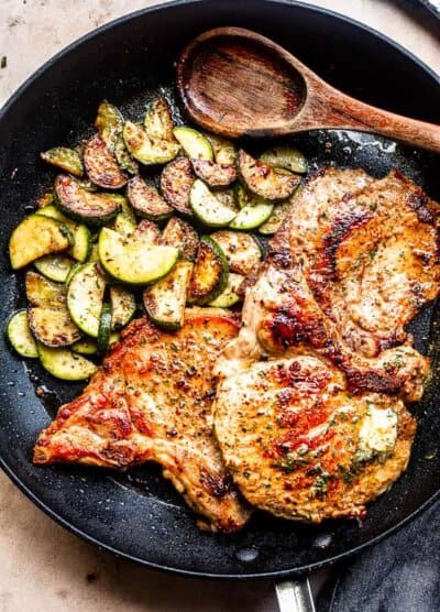 cooked sliced zucchini and cooked pork chops in a skillet with wooden spoon to the side