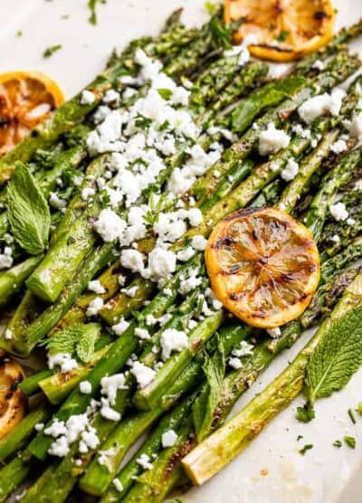 side close up shot of asparagus sprinkled with feta cheese and slices of lemon