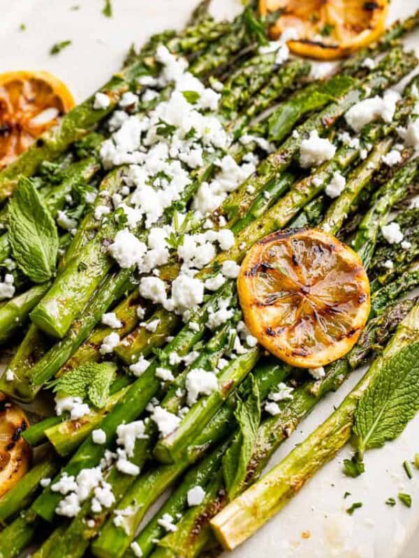 side close up shot of asparagus sprinkled with feta cheese and slices of lemon
