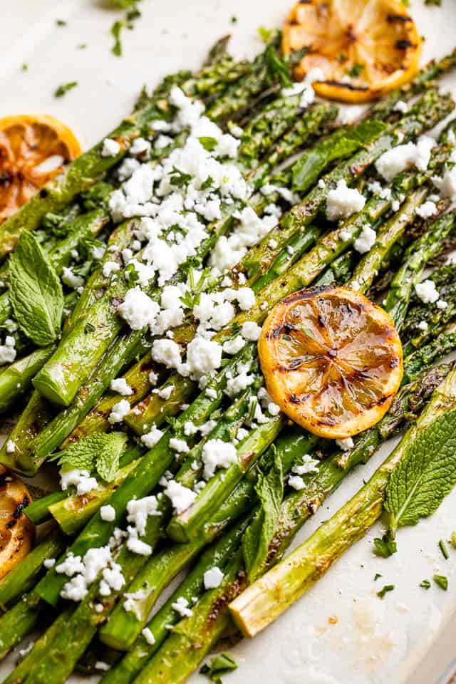 side close up shot of asparagus sprinkled with feta cheese and slices of lemon