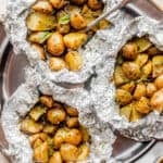 top view of a pewter plate with three foil packets filled with basil pesto brushed potatoes