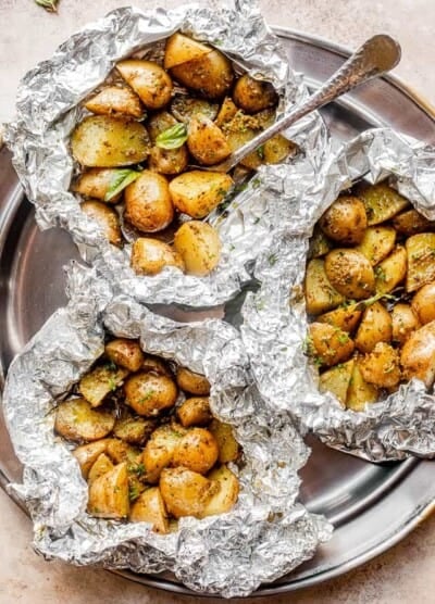 top view of a pewter plate with three foil packets filled with basil pesto brushed potatoes