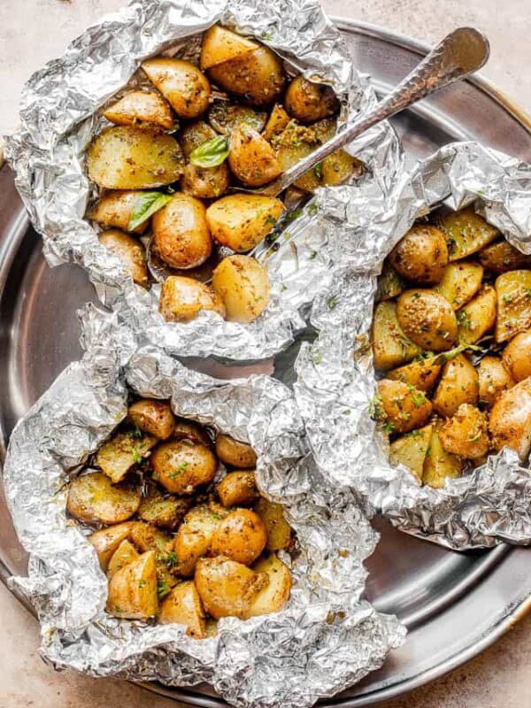 top view of a pewter plate with three foil packets filled with basil pesto brushed potatoes