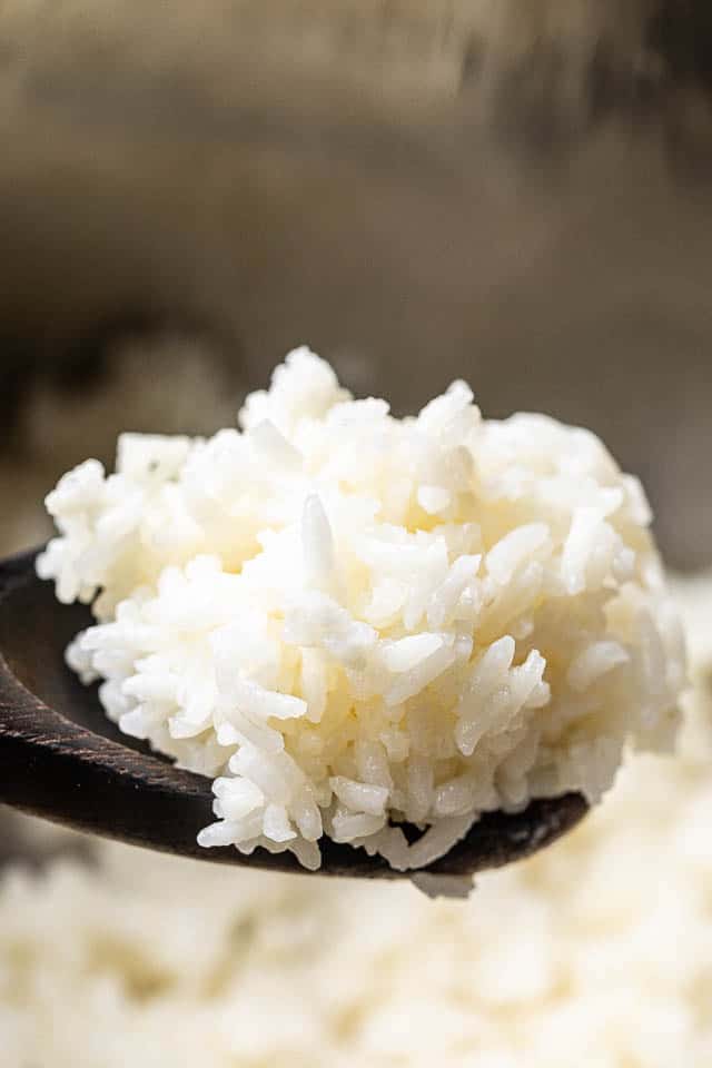 heaping scoop of cooked jasmine rice in a brown wooden spoon