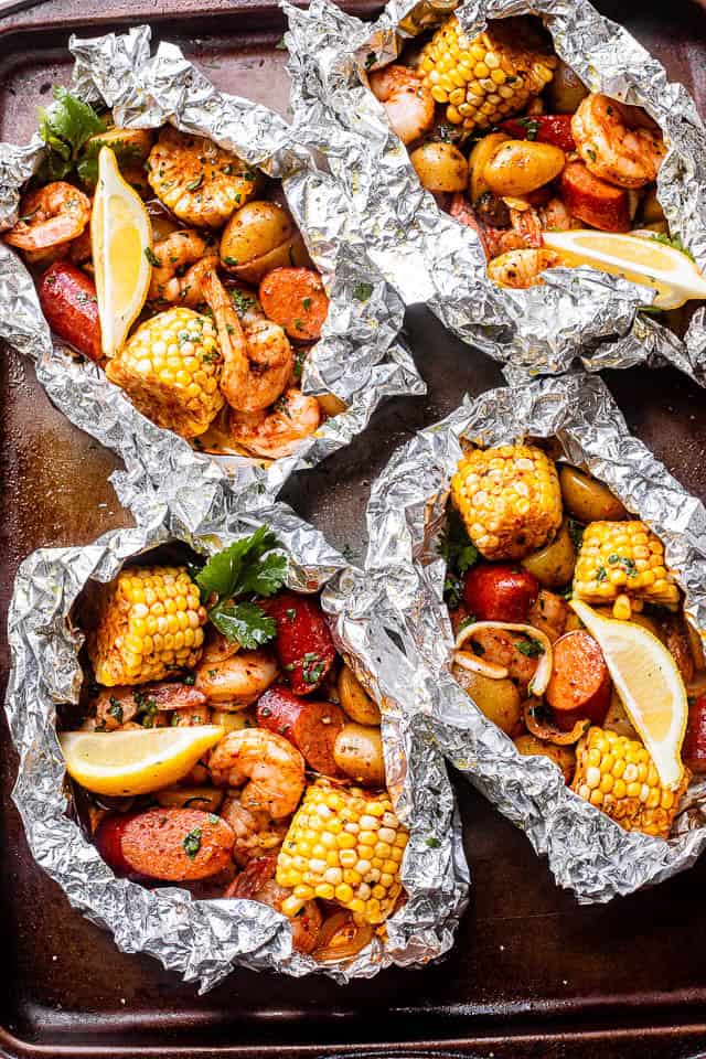 Shrimp boil in foil packets arranged on top of a baking sheet.