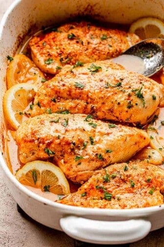 baked chicken breasts set over lemon slices in a baking dish