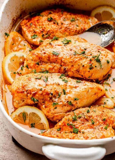 baked chicken breasts set over lemon slices in a baking dish