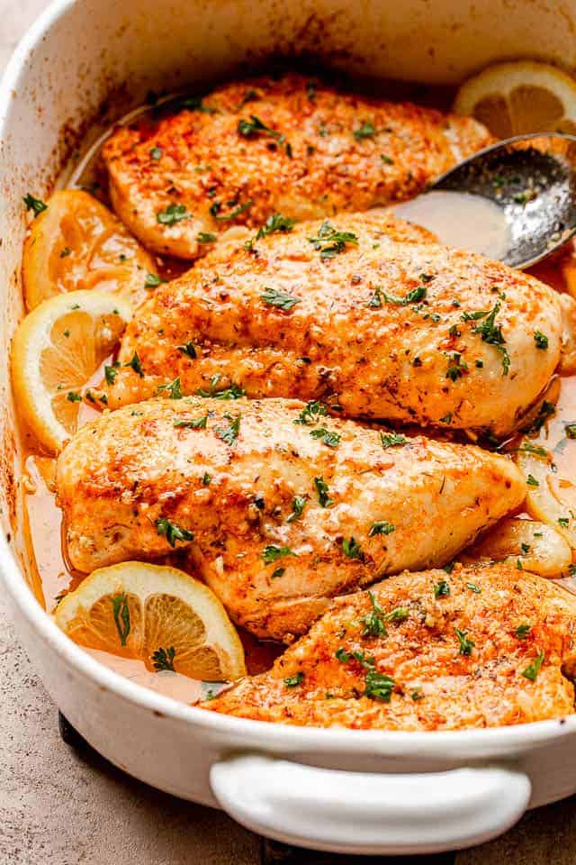 Baked chicken breasts set over lemon slices in a baking dish.