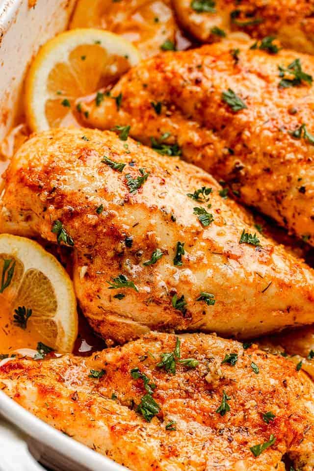 close up shot of lemon baked chicken breasts sprinkled with parsley and garnished with lemon slices