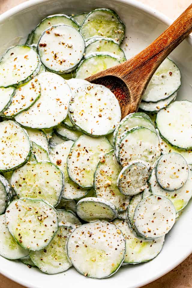 cucumber slices in a white salad bowl tossed with creamy dressing