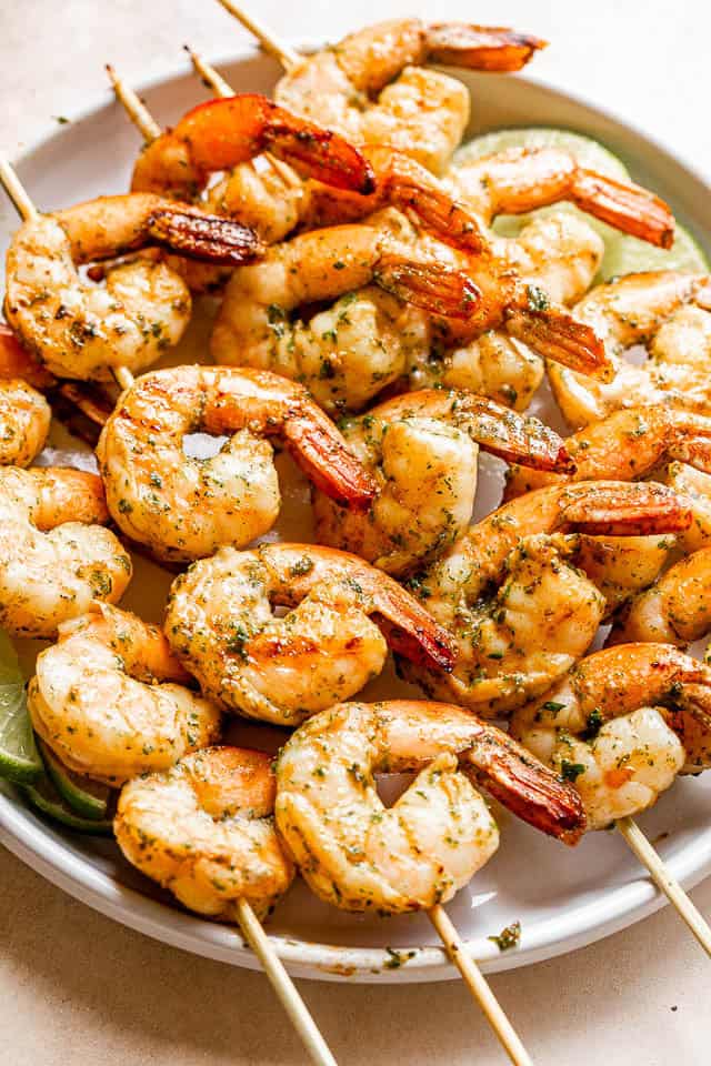 This grilled shrimp recipe is quick, easy, and delicious! Juicy, tender shrimp are marinated with garlic, basil, and lime and then grilled in minutes. Perfect for summer cookouts or an easy dinner. Grilled shrimp threaded onto skewers and arranged on a plate.