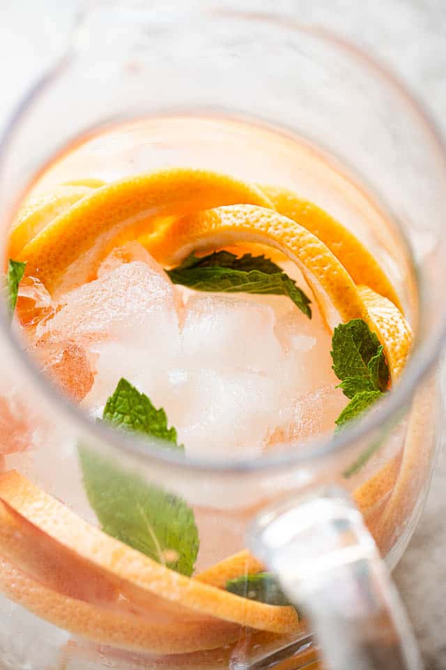 above shot of a glass pitcher filled with ice, grapefruit slices, and mint leaves