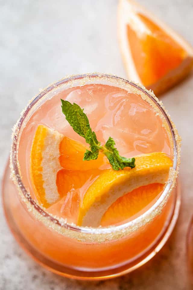top view of a cocktail glass with ice, orange drink, grapefruit slices, and mint