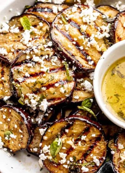 close up shot of eggplant slices in a bowl set next to a garlic vinaigrette and topped with crumbled feta cheese
