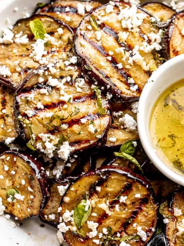 close up shot of eggplant slices in a bowl set next to a garlic vinaigrette and topped with crumbled feta cheese