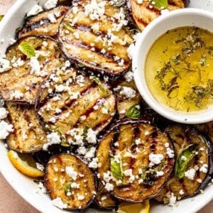 slices of grilled eggplant in a bowl set next to a garlic vinaigrette and topped with crumbled feta cheese