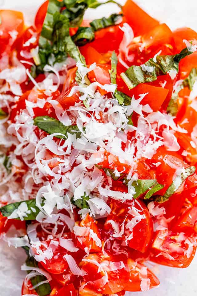 glass bowl with chopped tomatoes, shredded parmesan, and fresh basil 
