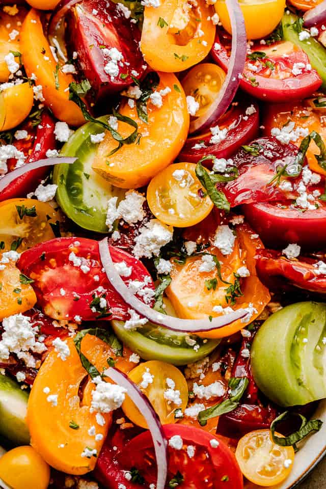 close up shot of wedges of colored tomatoes topped with slices of red onions and crumbled feta cheese