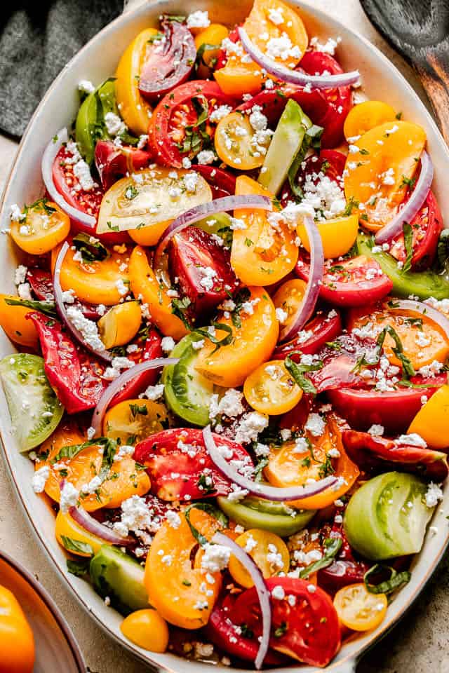 top shot of wedges of heirloom tomatoes in an oblong salad bowl topped with slices of red onions and crumbled feta cheese