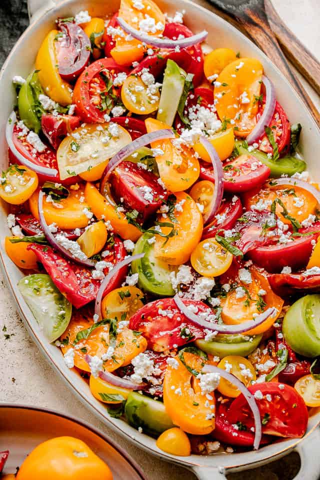 wedges of colored tomatoes topped with slices of red onions and crumbled feta cheese